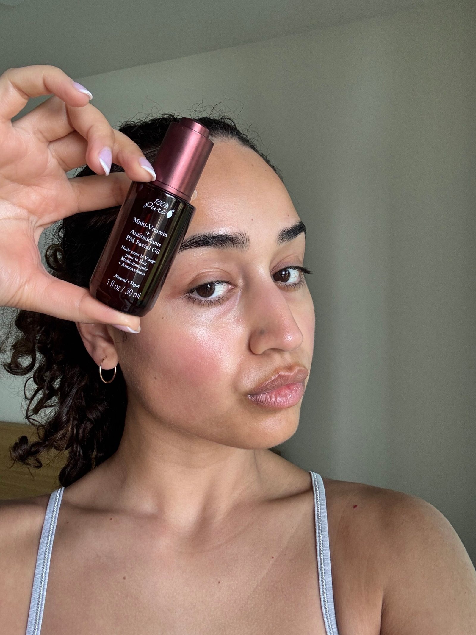A person holds a bottle of Kiehl’s Midnight Recovery Concentrate close to their face, showing glowing skin in a well-lit room.