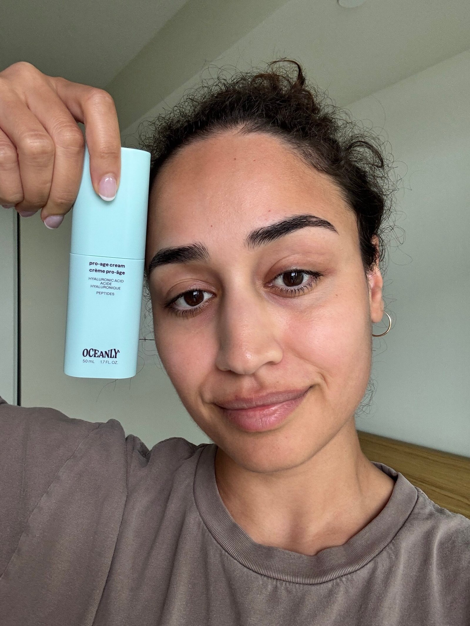 A person holds a light blue Oceanly skincare product next to their face, looking at the camera with a neutral expression.