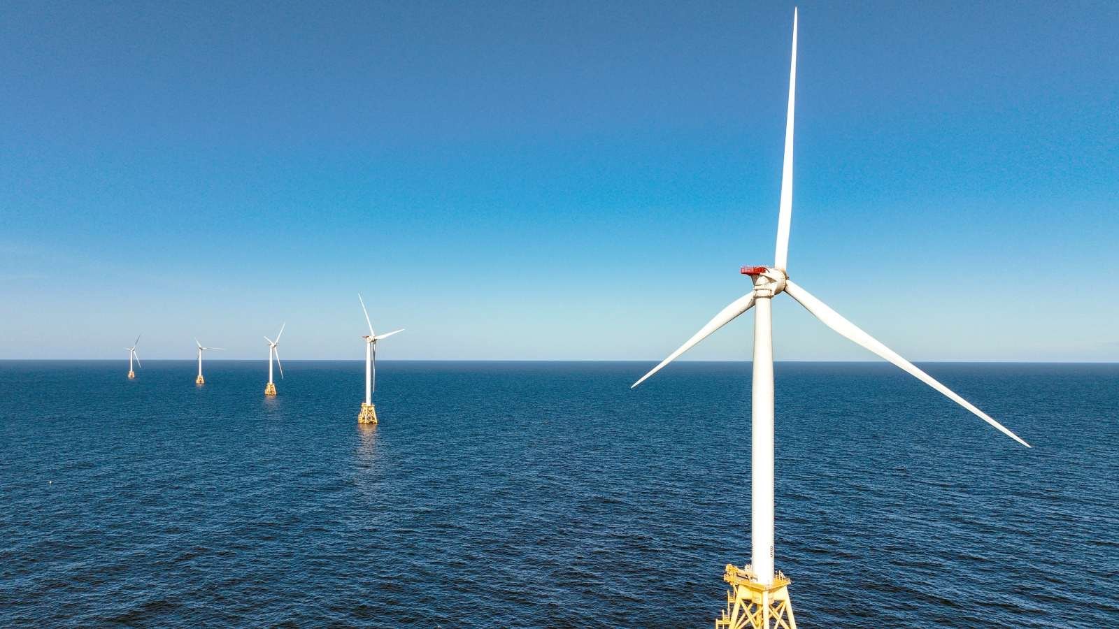 White wind turbines stand in the middle of the ocean