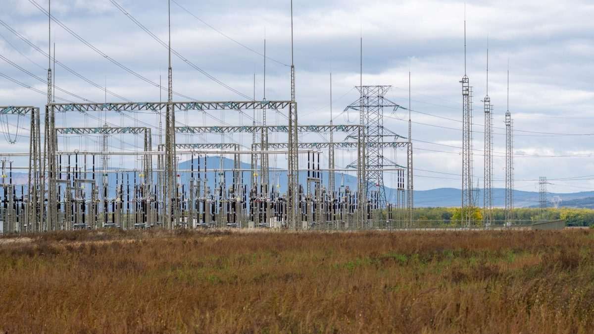 Electrical substation and high-voltage transmission towers beneath an overcast sky.