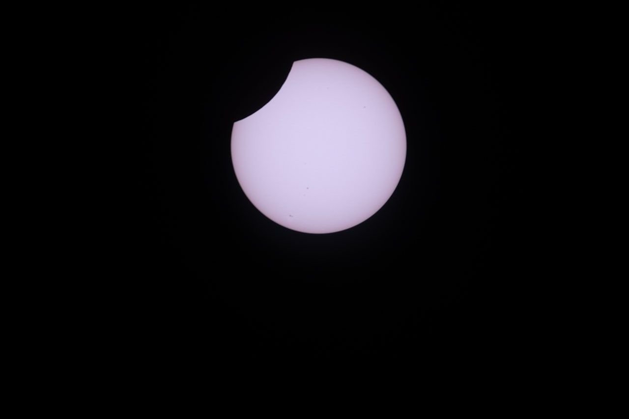 A photo shows the partially eclipsed Sun as a white disk, set against a black sky, with a small