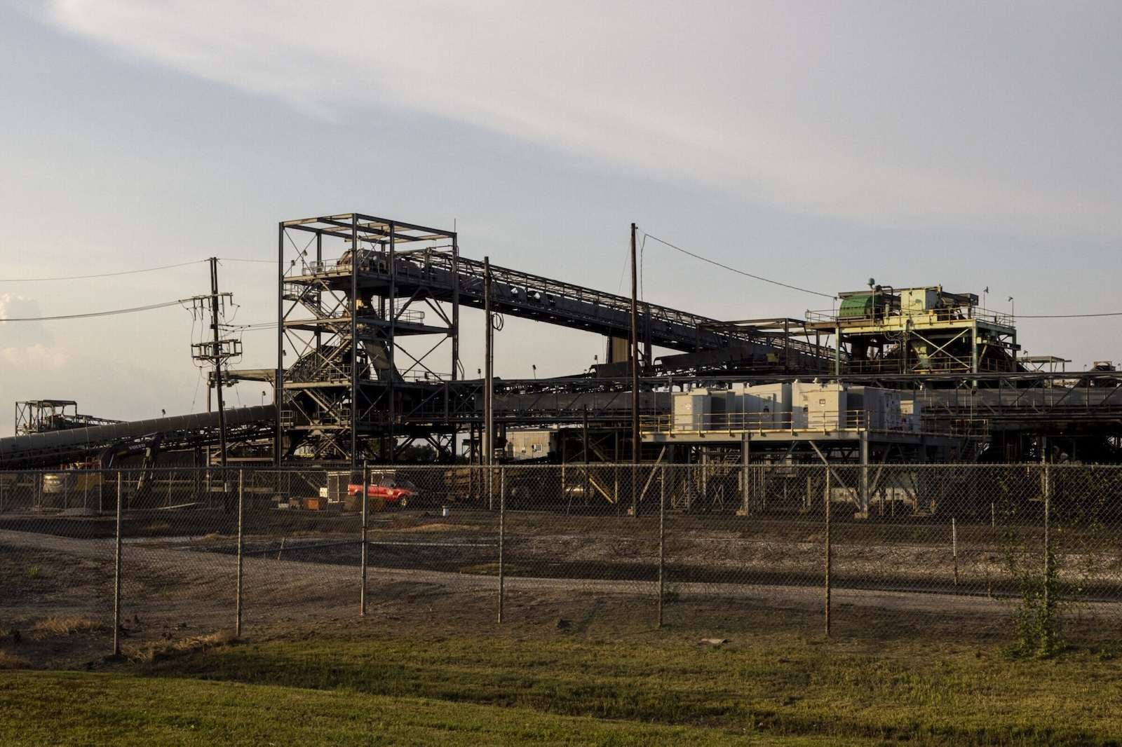 A large industrial structure sits behind a chainlink fence