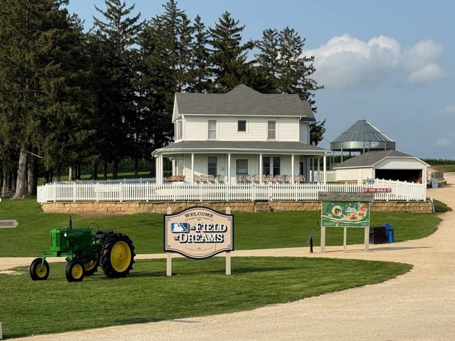 A green John Deere tractor sits on the lawn below the white two-storey farmhouse with a wraparound porch and white picket fence made famous by the film. Photo: Dave McEachren