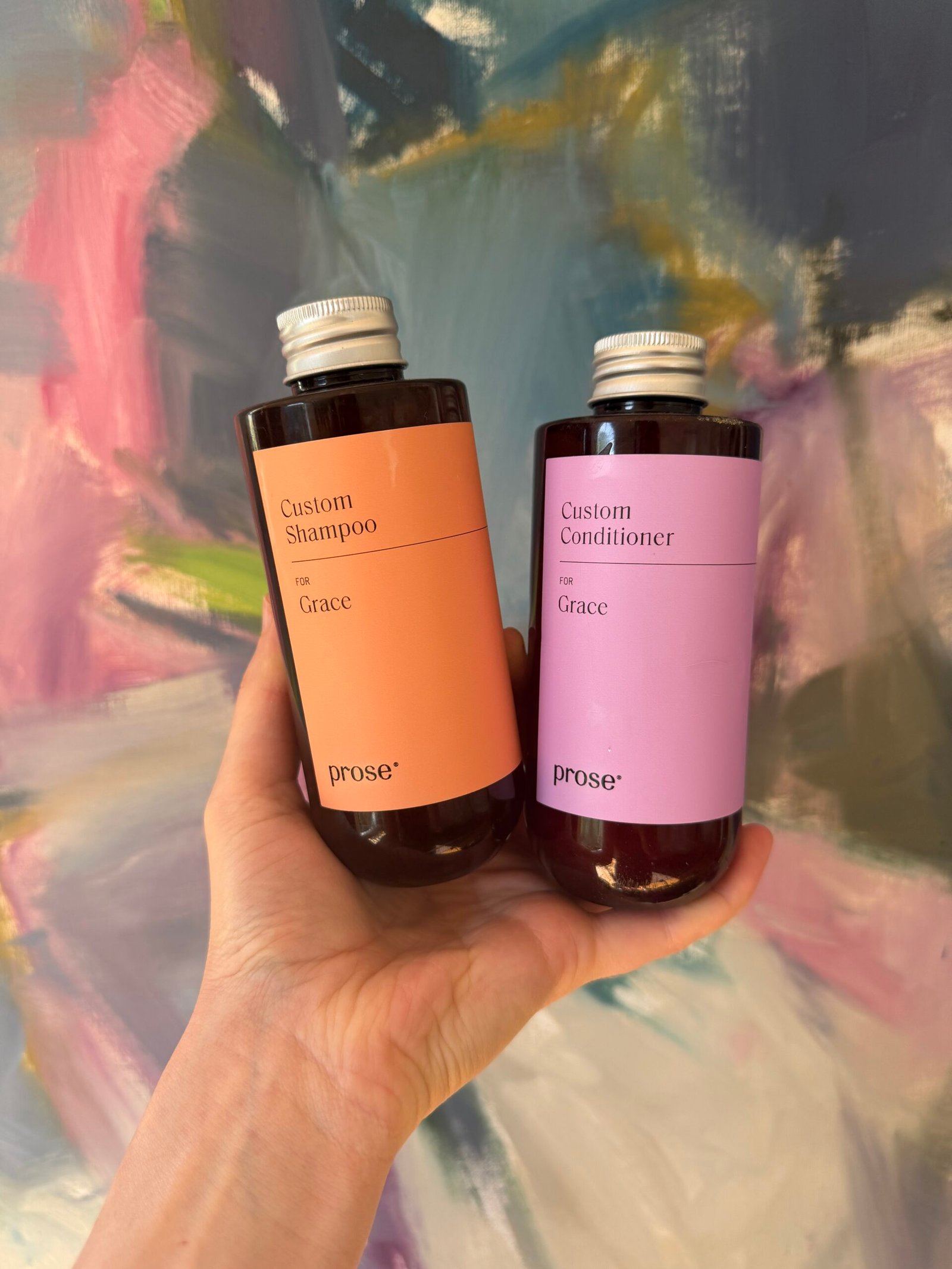 A hand holds two bottles labeled “Custom Shampoo for Grace” and “Custom Conditioner for Grace” against a colorful abstract background.