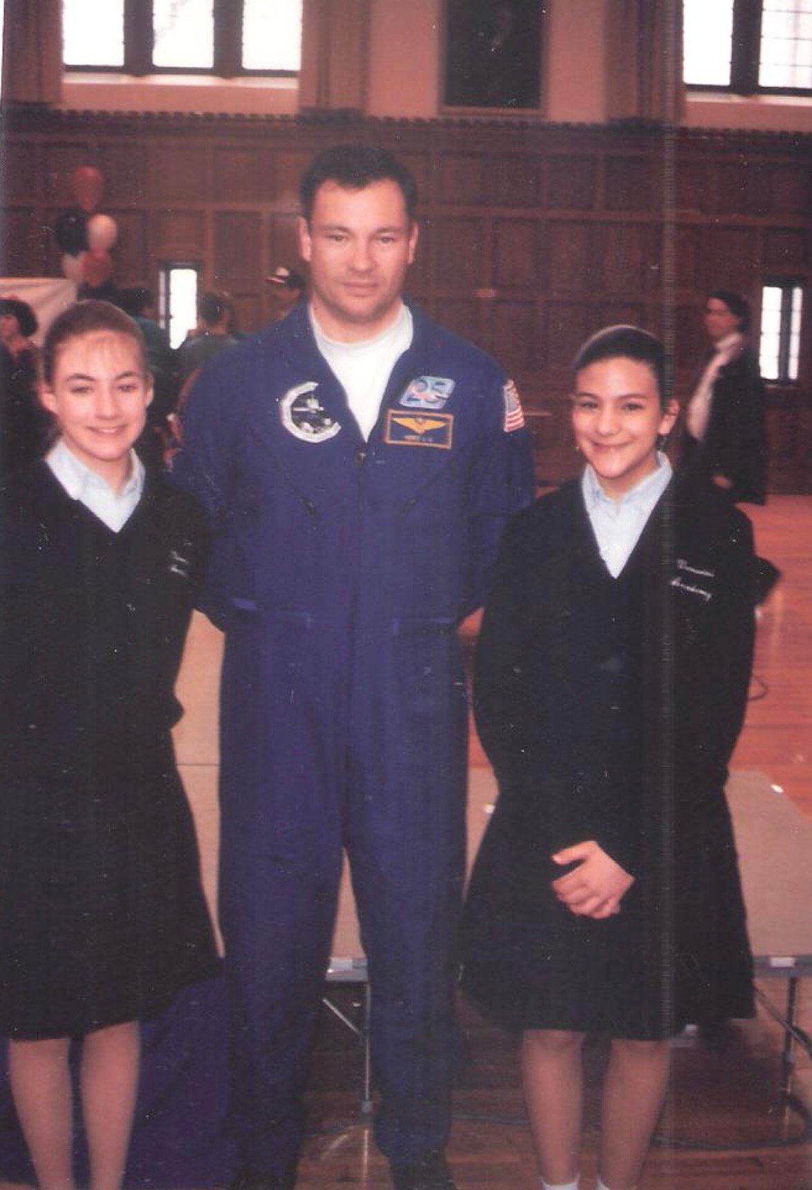 The photo features two young ladies in black dresses posing for a photograph with a NASA astronaut Michael Lopez-Alegria standing in the middle between the two young ladies.