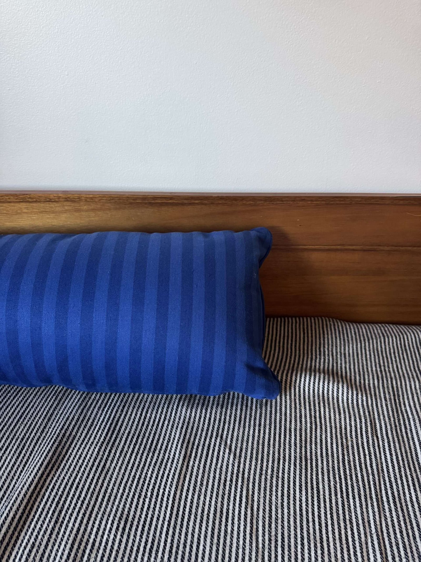 A blue striped pillow rests against a wooden headboard on a bed with a black and white striped blanket.