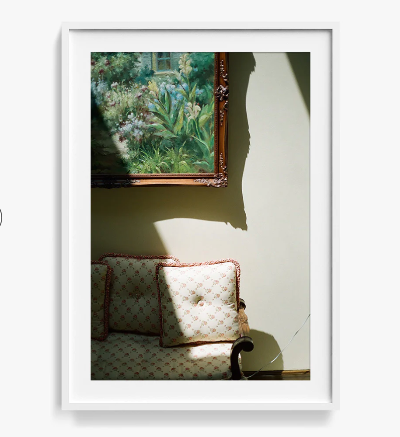 A framed photo of the edge of a couch and corner of a framed painting.