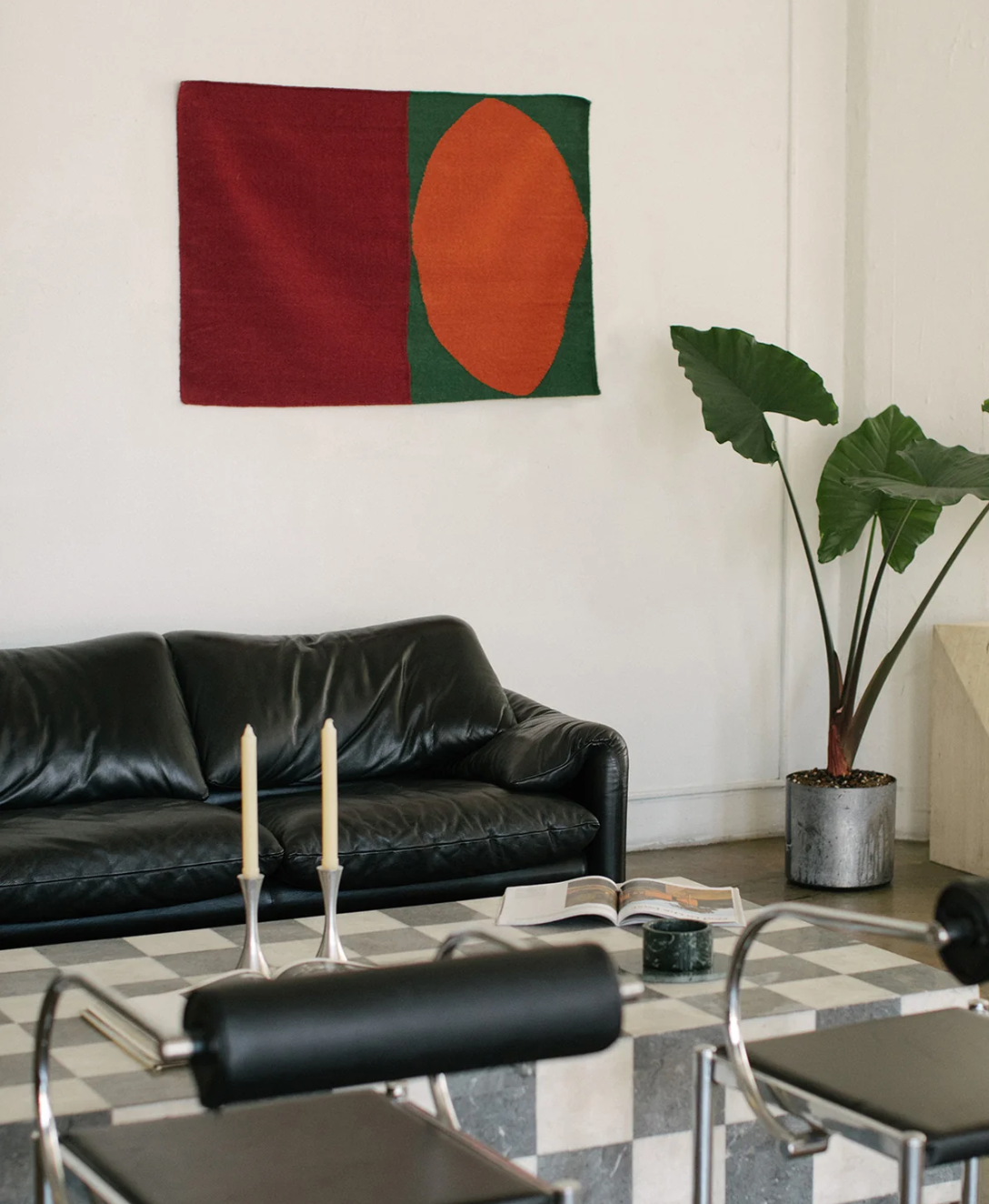 A bold red, green, and orange geometric textile hangs on the wall of a styled room.
