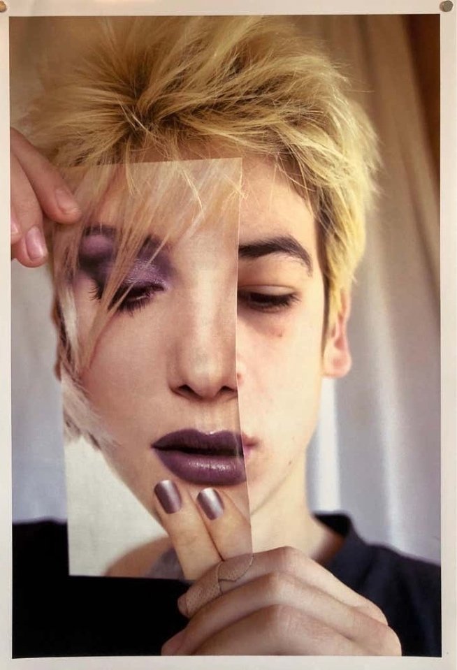 Person holds a magazine page of a made-up face over their own, aligning the features to blend the two faces together.