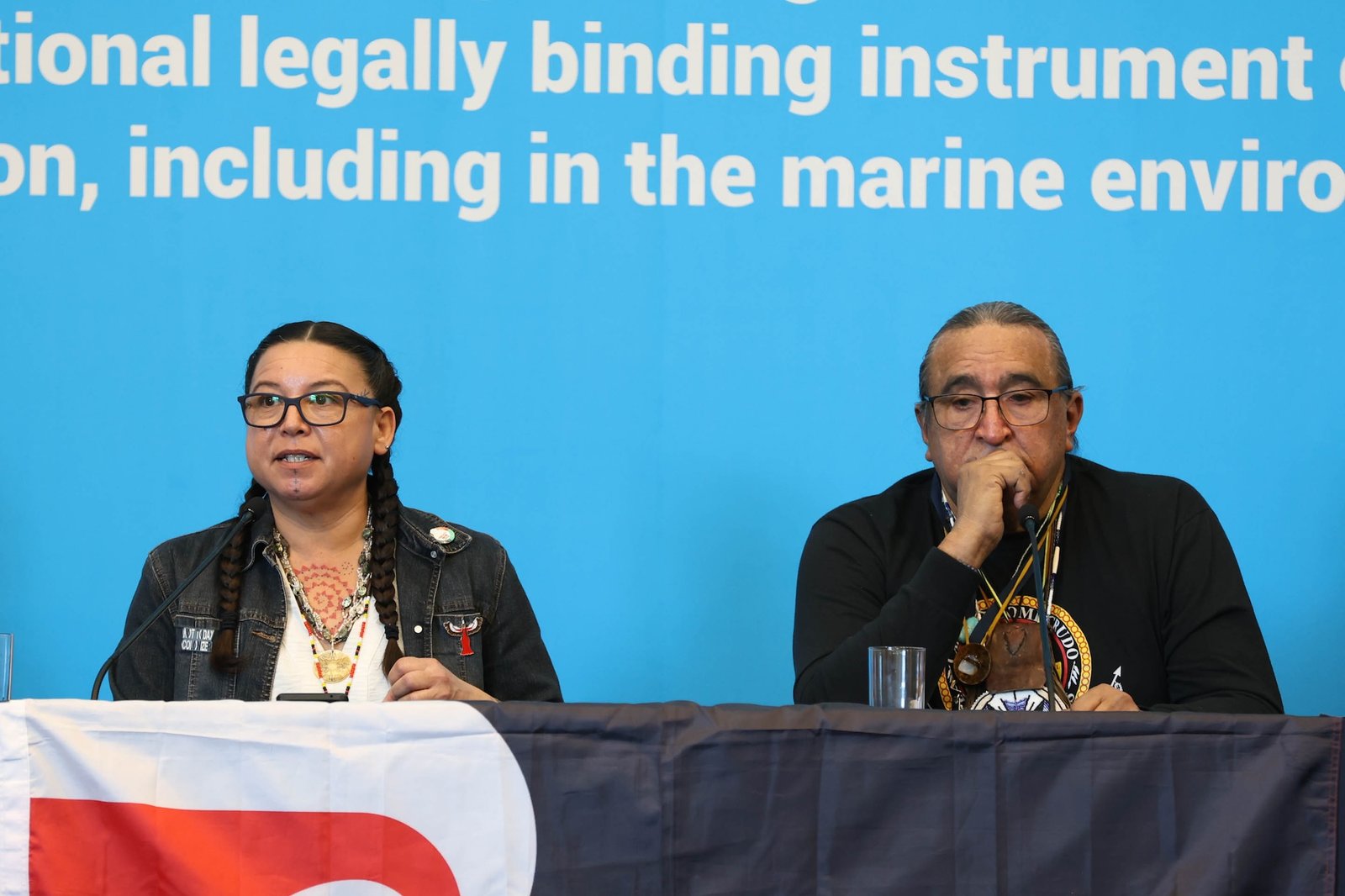 A woman and Juan Mancias sit on a panel in front of a bright blue backdrop