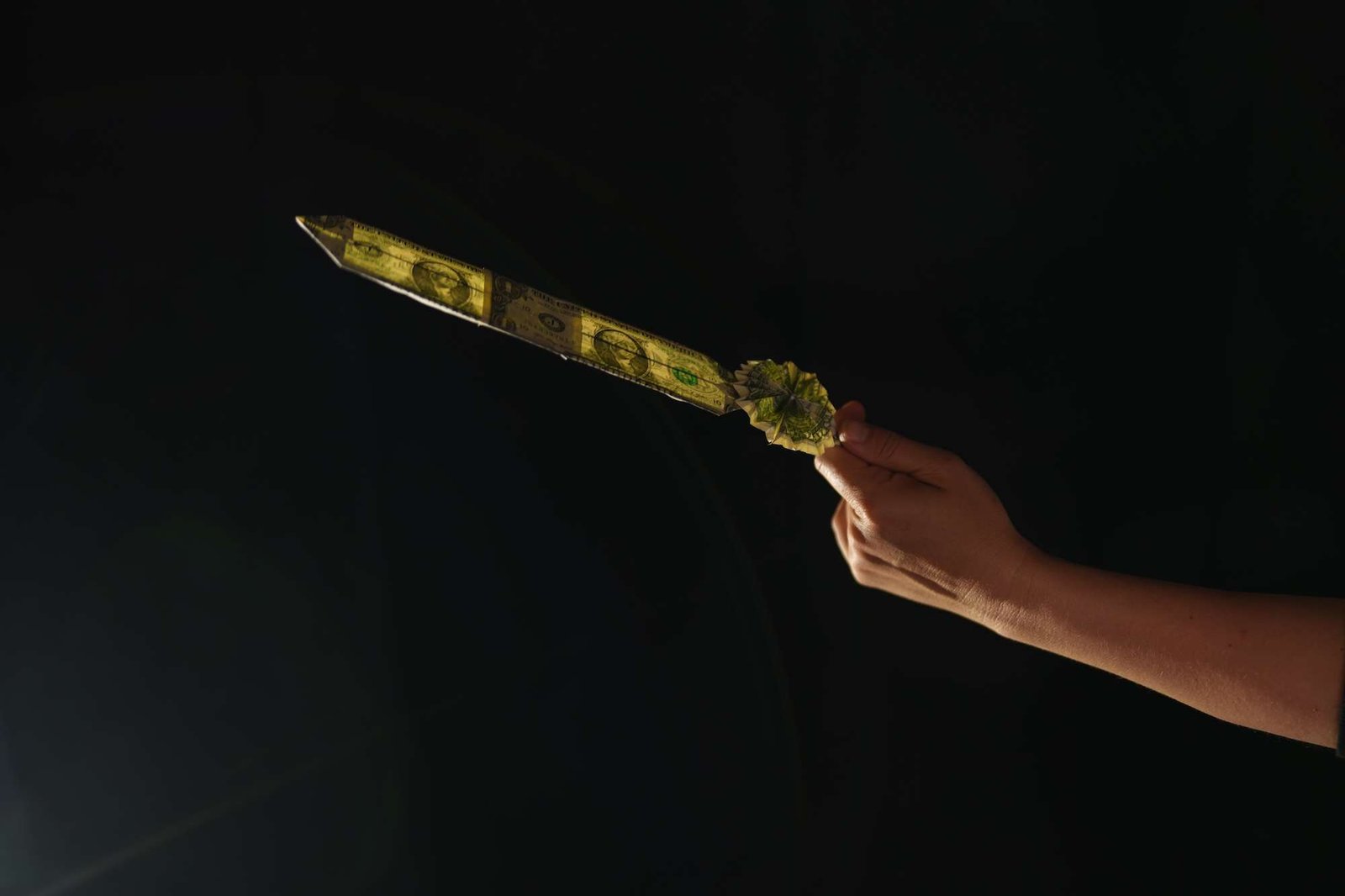 A hand holds out a feather made of two dollars folded bills