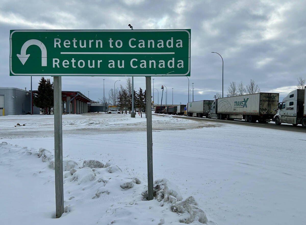 Transport trucks queue at a Canadian border crossing beside a Return to Canada sign. Photo: Robert Arnason