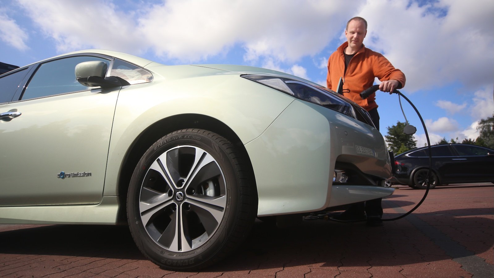 A man plugs a charger into an electric vehicle in a driveway