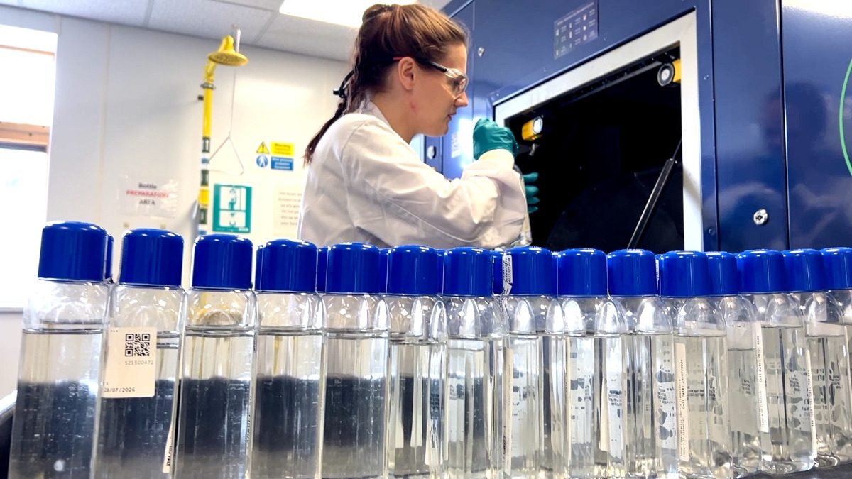 Laboratory worker loading plastic sample bottles into an industrial processing machine.