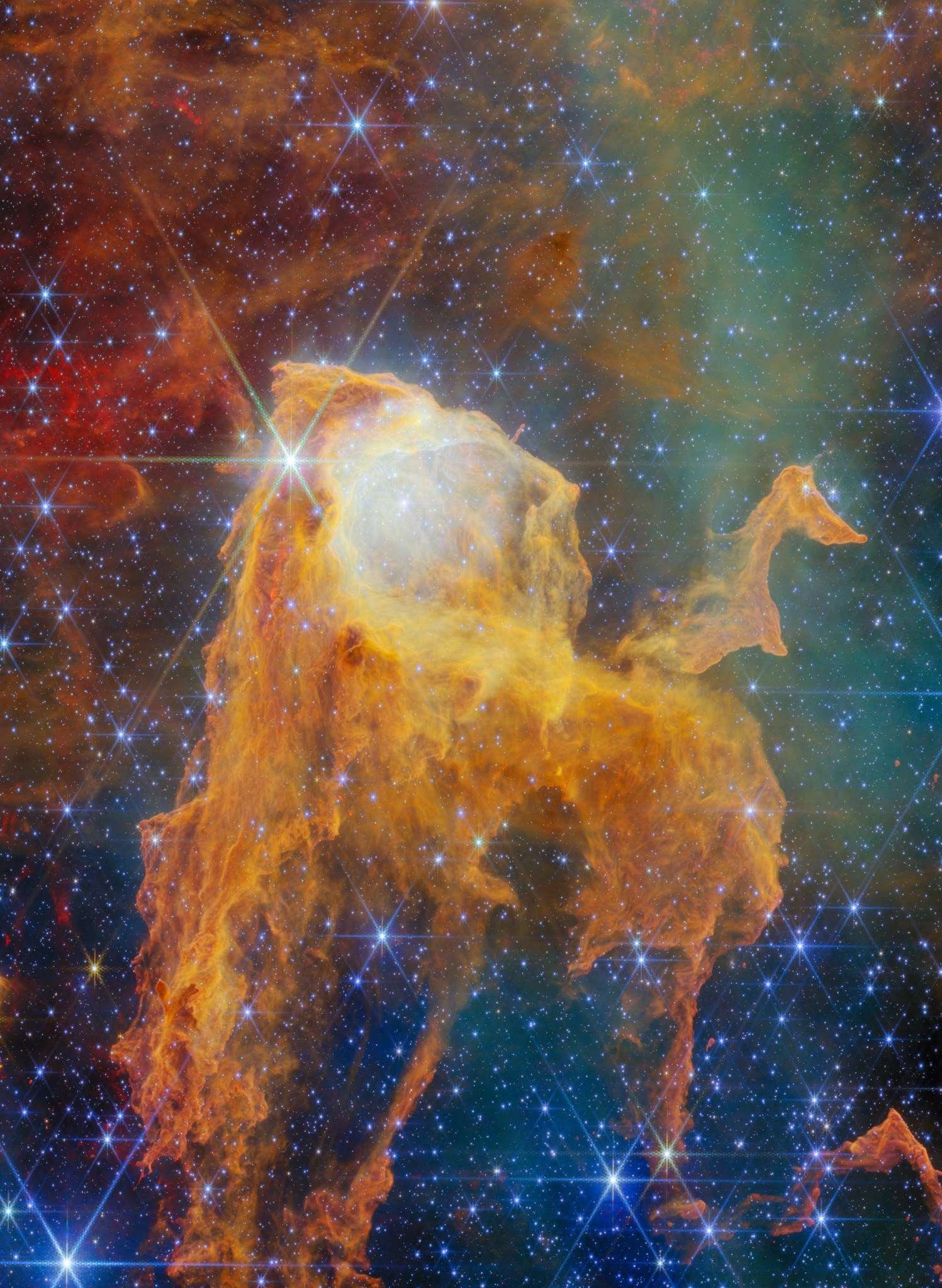 A region of space filled with bright stars and clouds of gas. In the center, the densest clouds form the shape of a chest with its lid open. The chest appears to glow from within. At its base it breaks apart into long pillars of thick gas. Many of the gas clouds in the background are dark orange globules, while others form large, pale hazes. A few brightly shining stars lie in the foreground, the biggest and brightest in front of the chest’s lid.