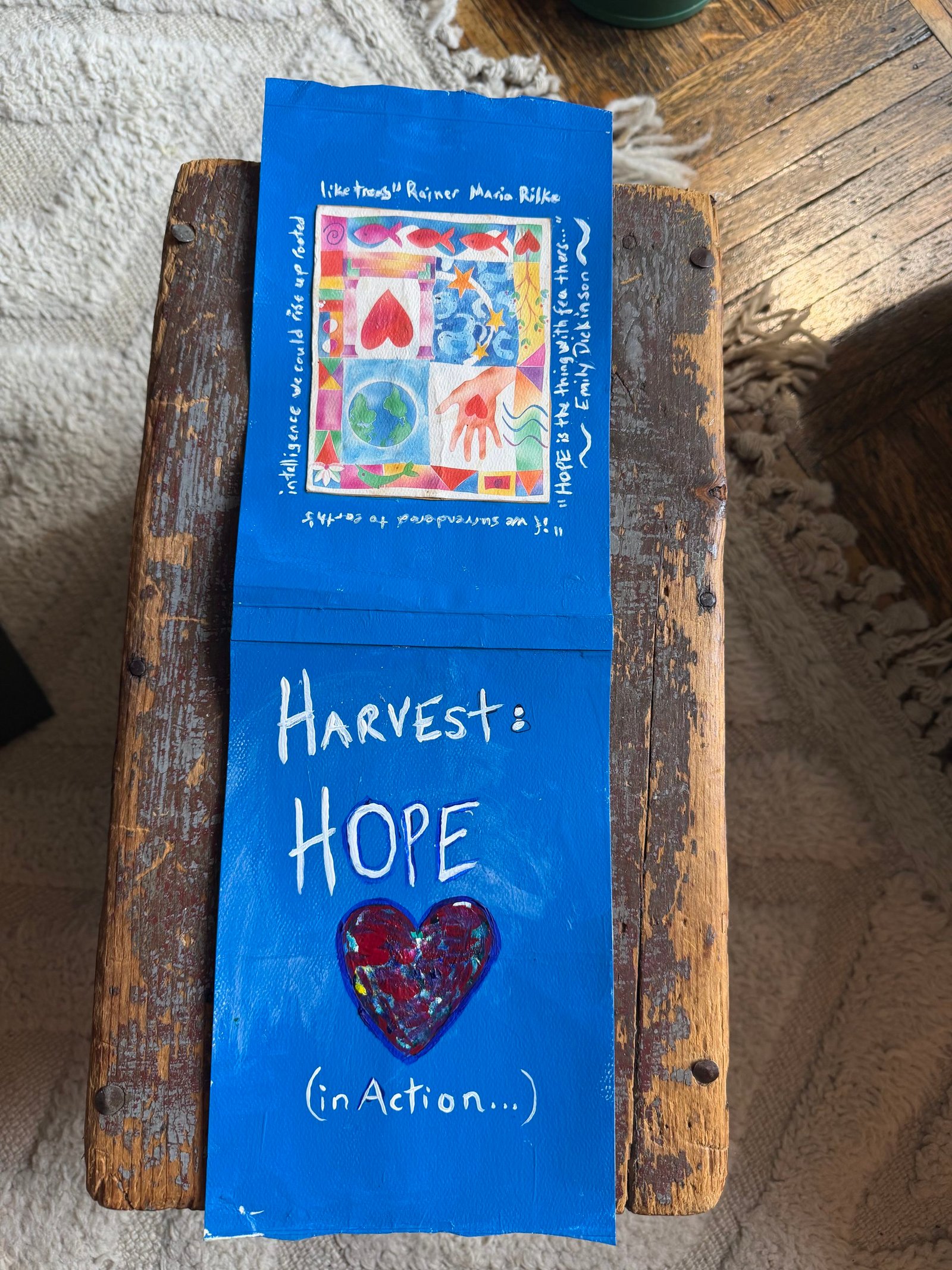 A handmade card on a wooden stool reads “HARVEST: HOPE (in Action...)” with a painted heart and a colorful artwork above, surrounded by handwritten text.