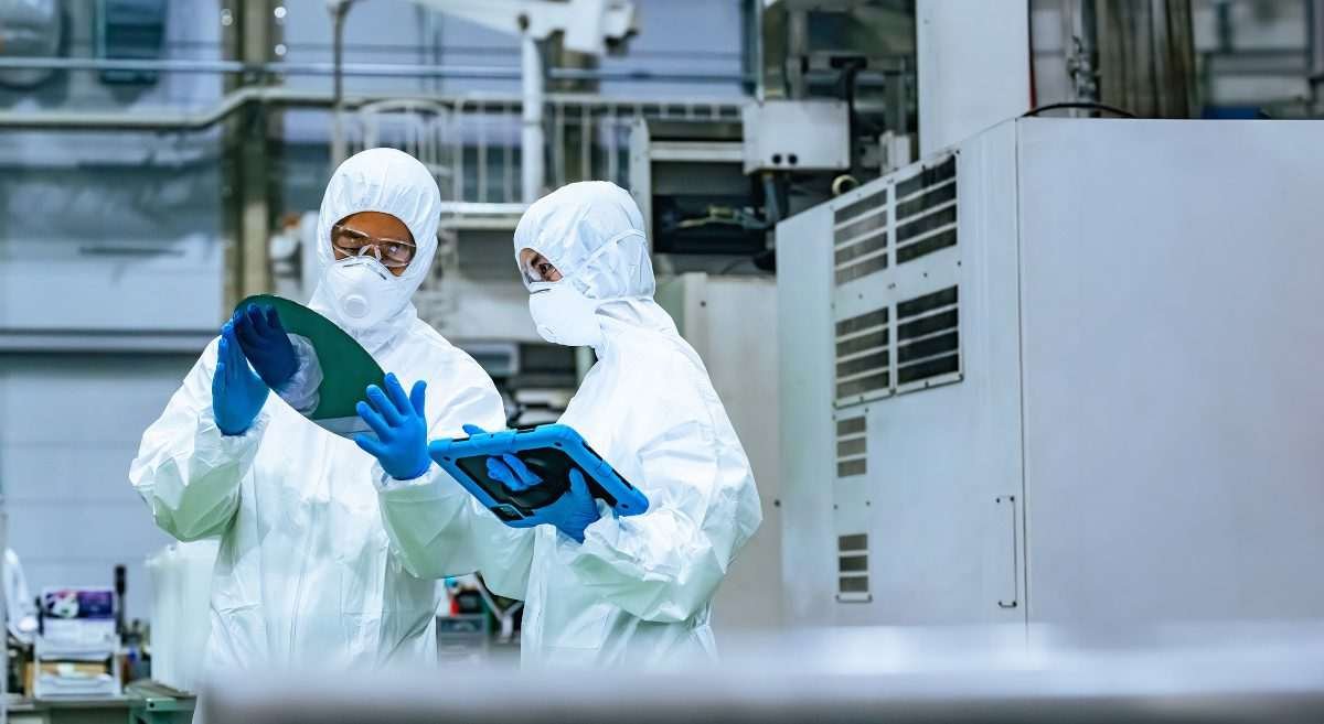 Workers in protective clothing inspect silicon wafers using a tablet in a semiconductor factory