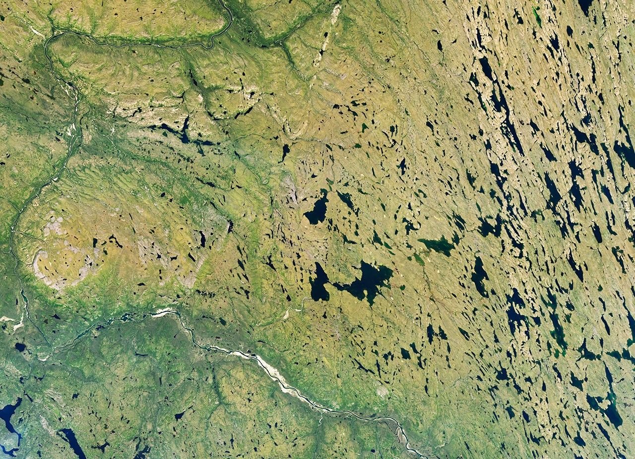 A river winds through a mostly green tundra landscape in summer, dotted with numerous lakes.