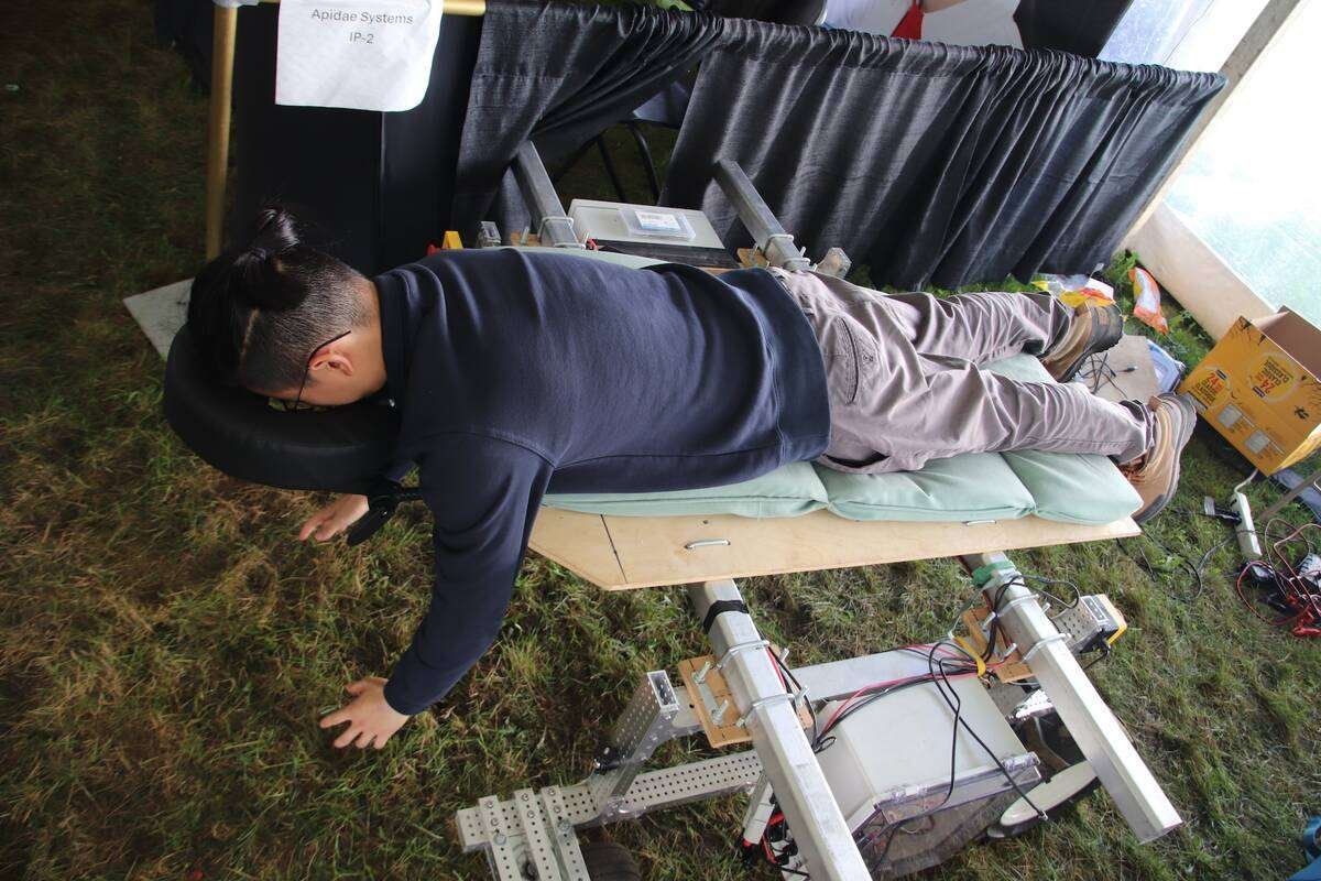 A man lies face down on the Taro Cobot with his face in a padded cradle and his arms hanging toward the grass. Photo: Jonah Grignon