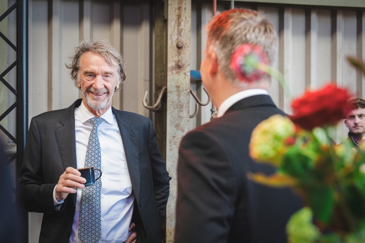 Sir Jim Ratcliffe holding a cup and speaking with another guest at the Greensand launch event