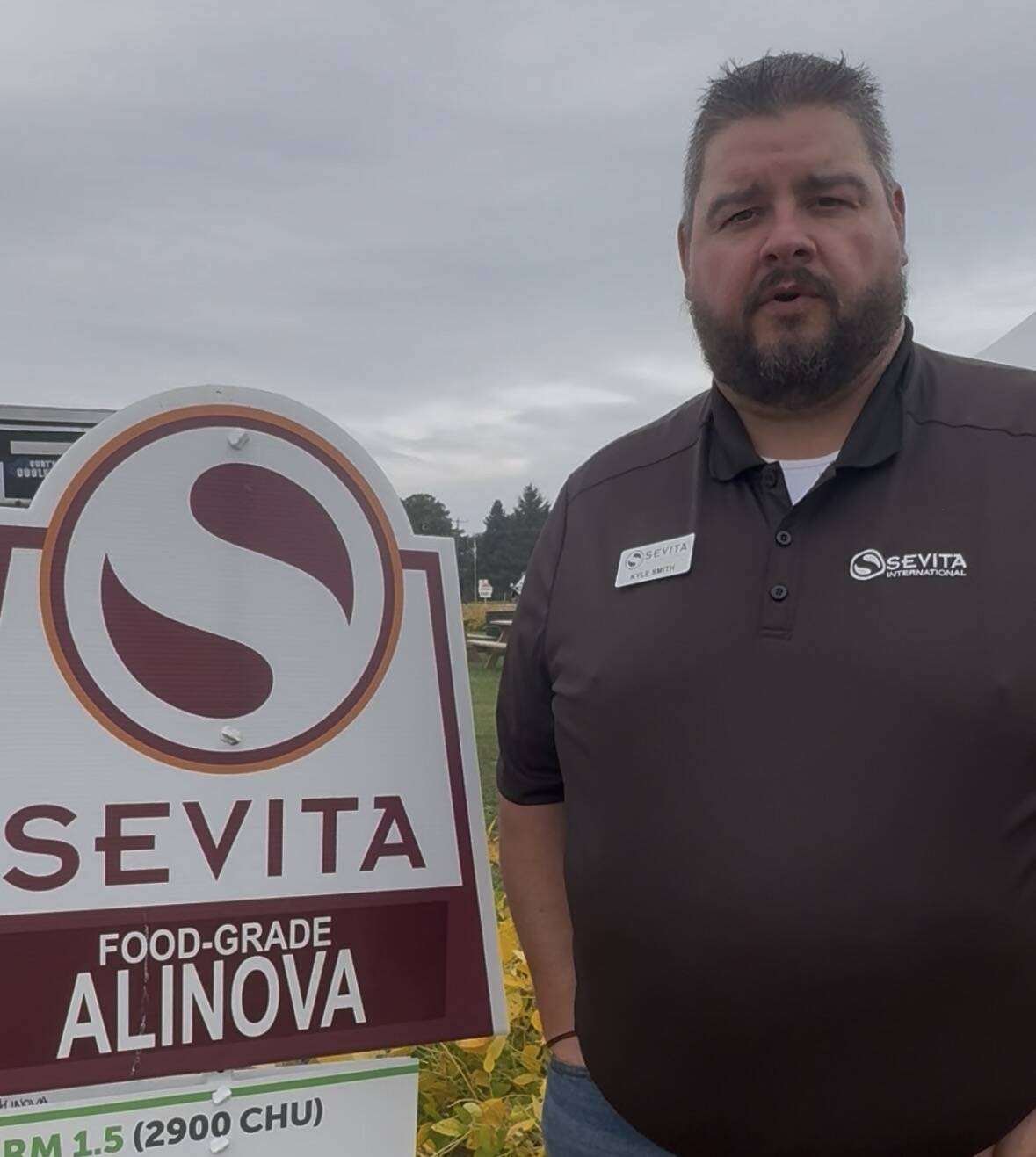 Kyle Smith of Sevita International, in a brown company polo, stands beside a Sevita Food-Grade Alinova plot sign under an overcast sky. Photo: Sarah McGoldrick
