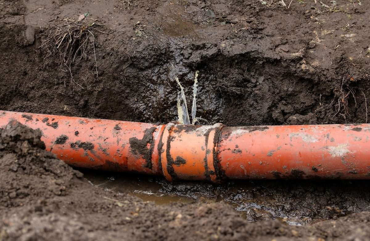 Water leaking from a damaged underground pipe exposed in a muddy trench