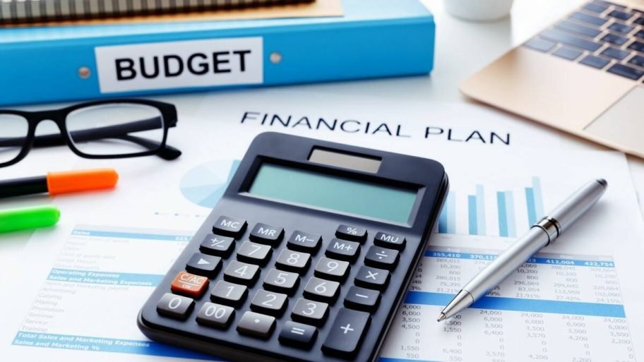 A calculator sitting on financial papers with a pair of glasses, a few markers, a pen and a binder that says "Budget" on it. Photo: Canva/Getty Images