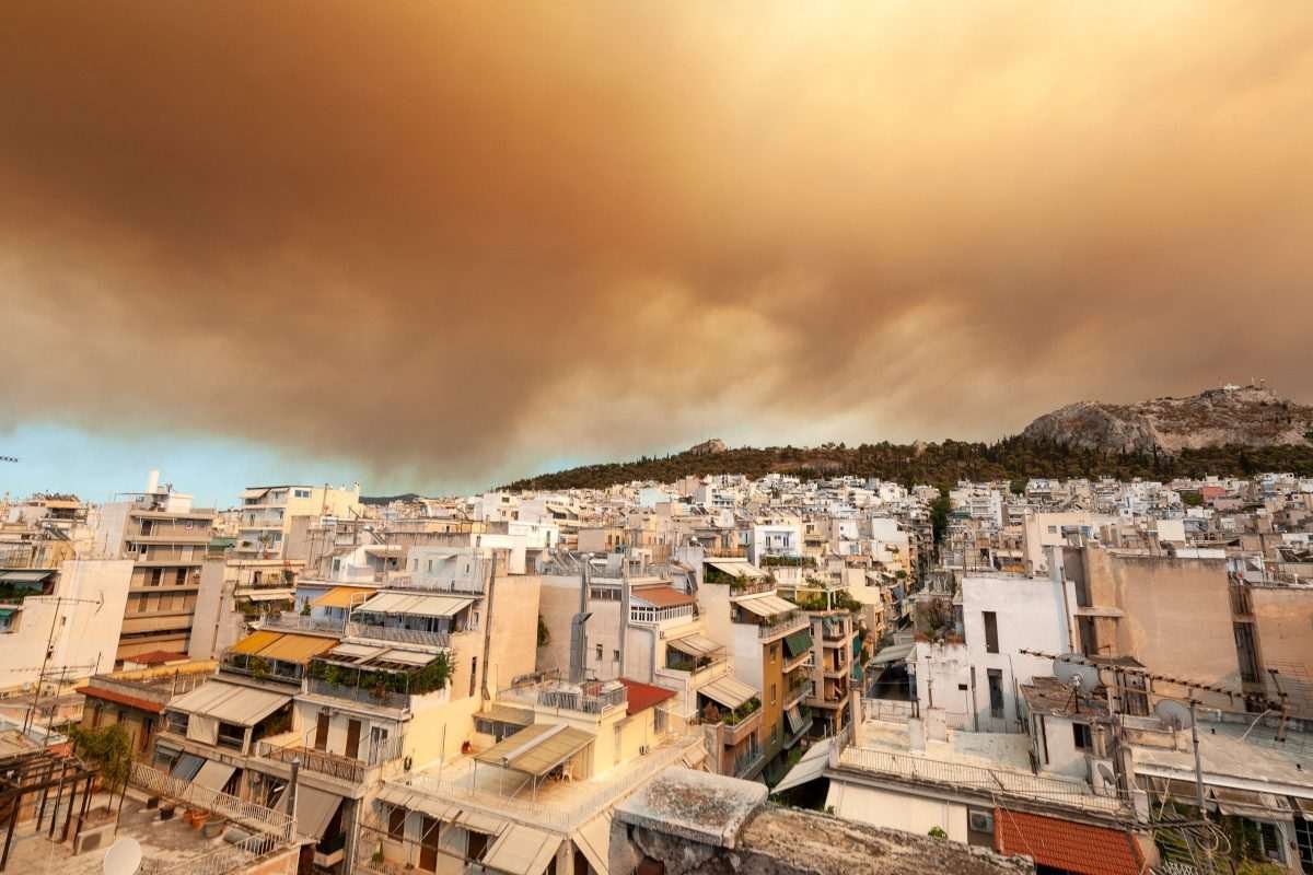 Dense brown wildfire smoke spreading across the sky above apartment buildings in Athens.