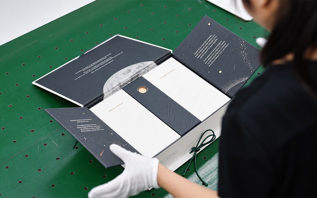 Artisan hands unfolding a rich, starry moonscape within a custom Mid-Autumn Packaging Design.