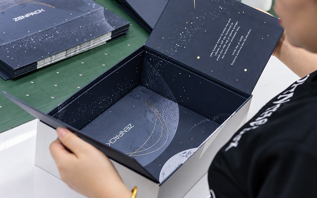 Hands opening a custom dark blue rigid gift box with printed moon and star artwork.