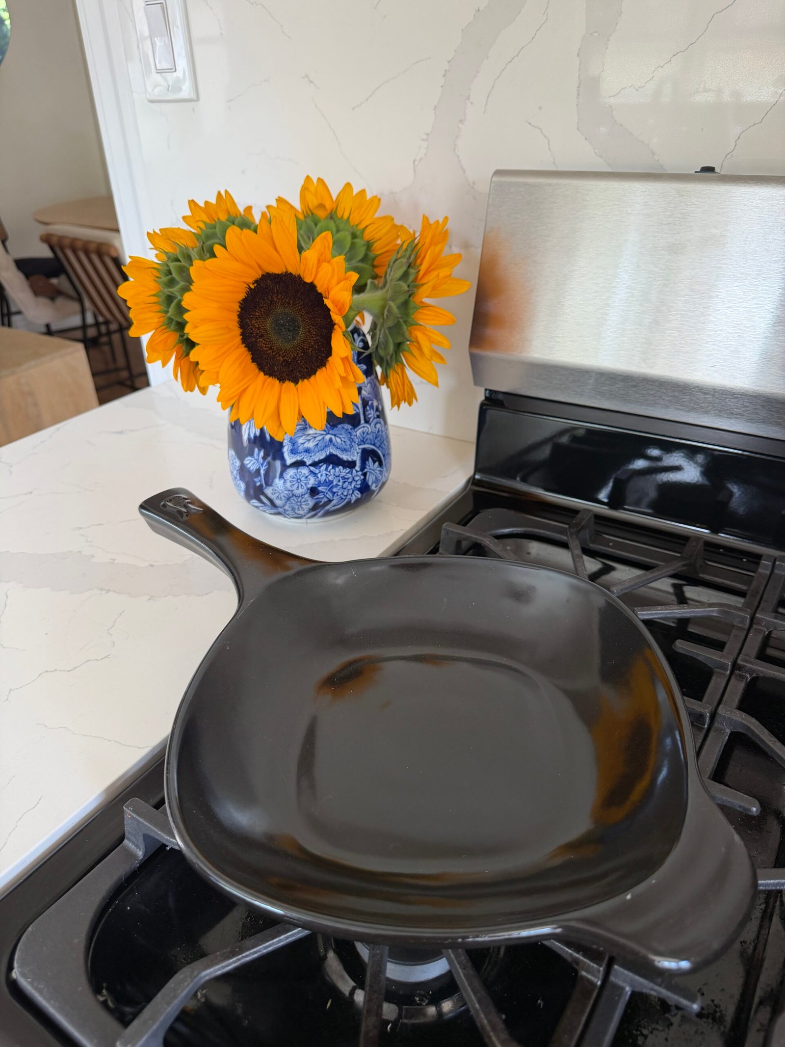 A black cast iron skillet sits on a stove, with a vase of sunflowers on the counter nearby.