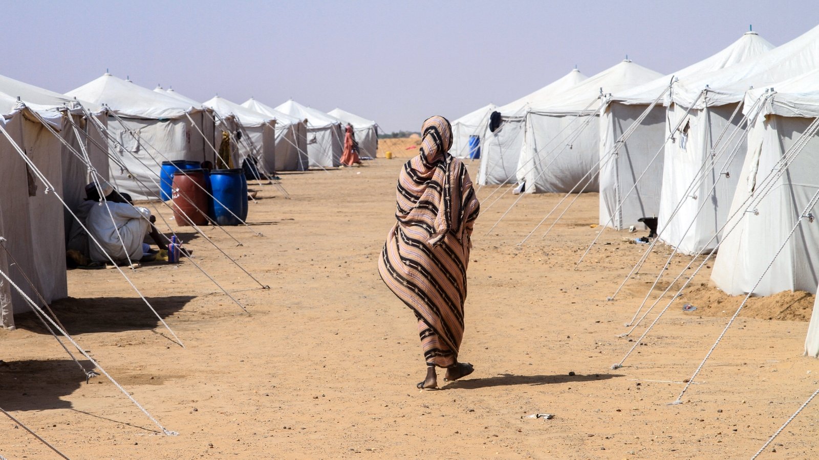 A woman walks alone among white tents in a desert