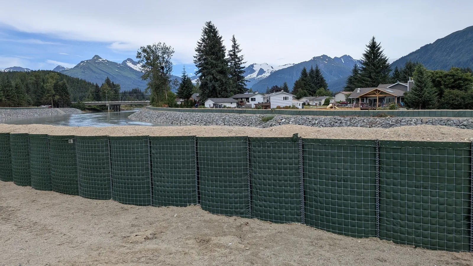 A green wall erected as a flood barrier stands between a river and the banks