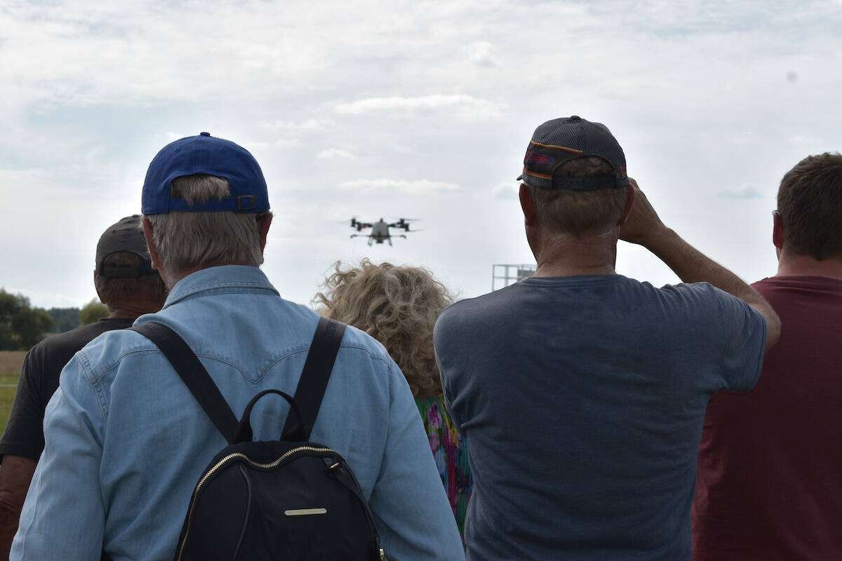 Visitors seen from behind watch a spray drone hover over the demo field. Photo: Canada's Outdoor Farm Show 2025