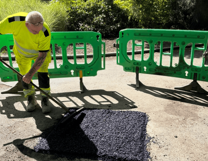 Worker applies a dark surfacing material to a pothole during a repair trial in Maidstone.