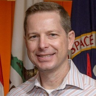 A portrait shot of Steve Ormsby in front of a NASA flag.