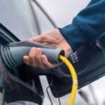 Man plugging in charger into an electric car at charge station