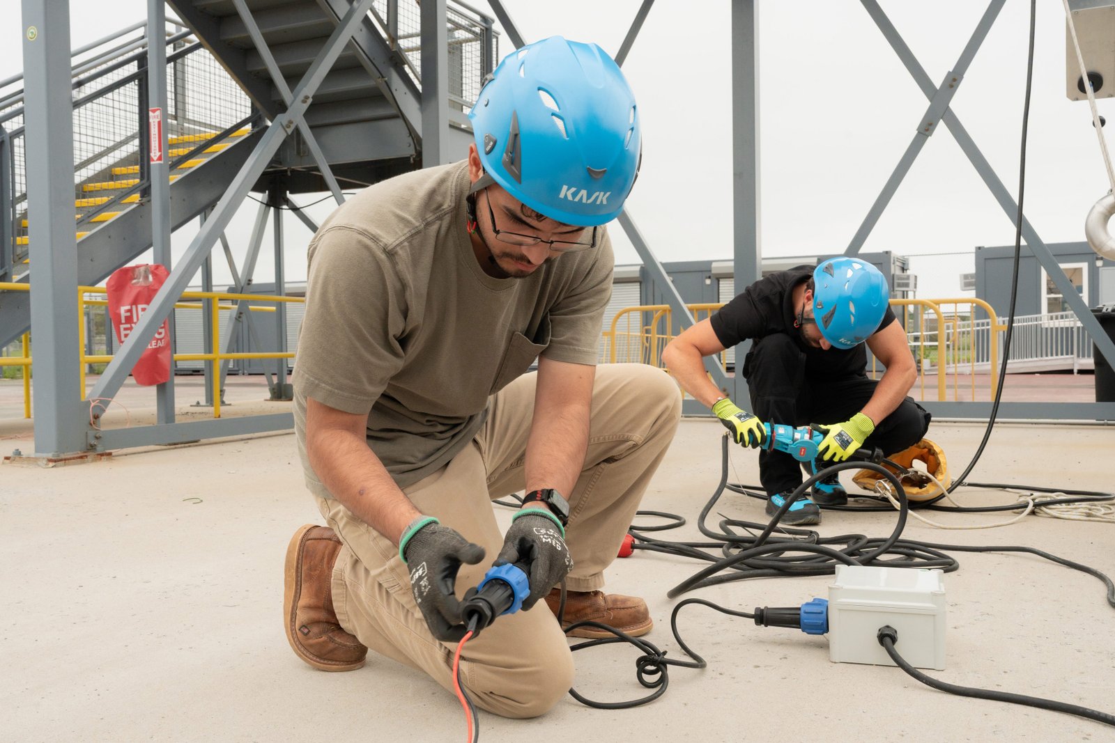 Two men in hard hats work work on an electrical line