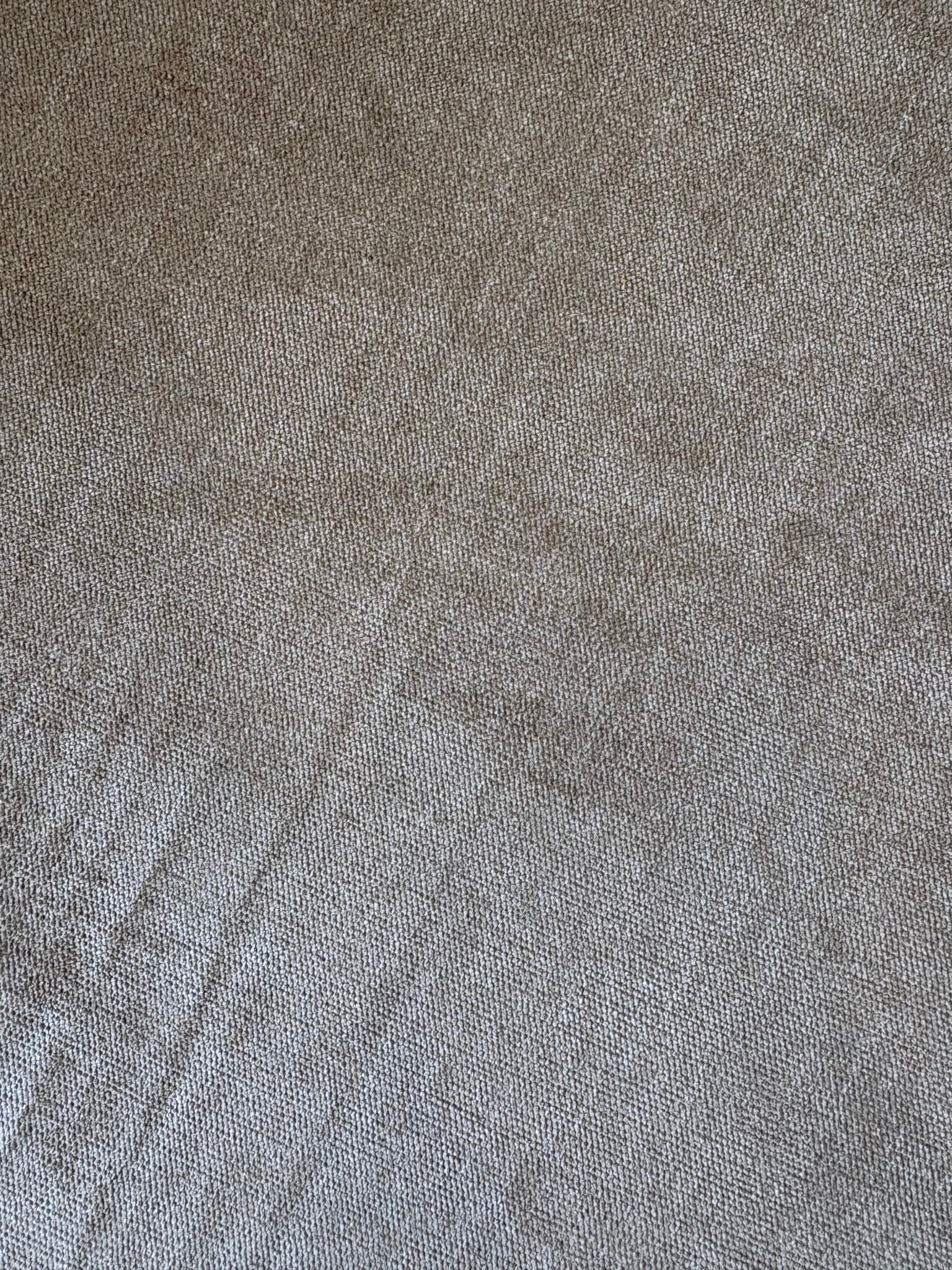 A close-up of beige textured fabric with visible weave patterns and subtle creases.