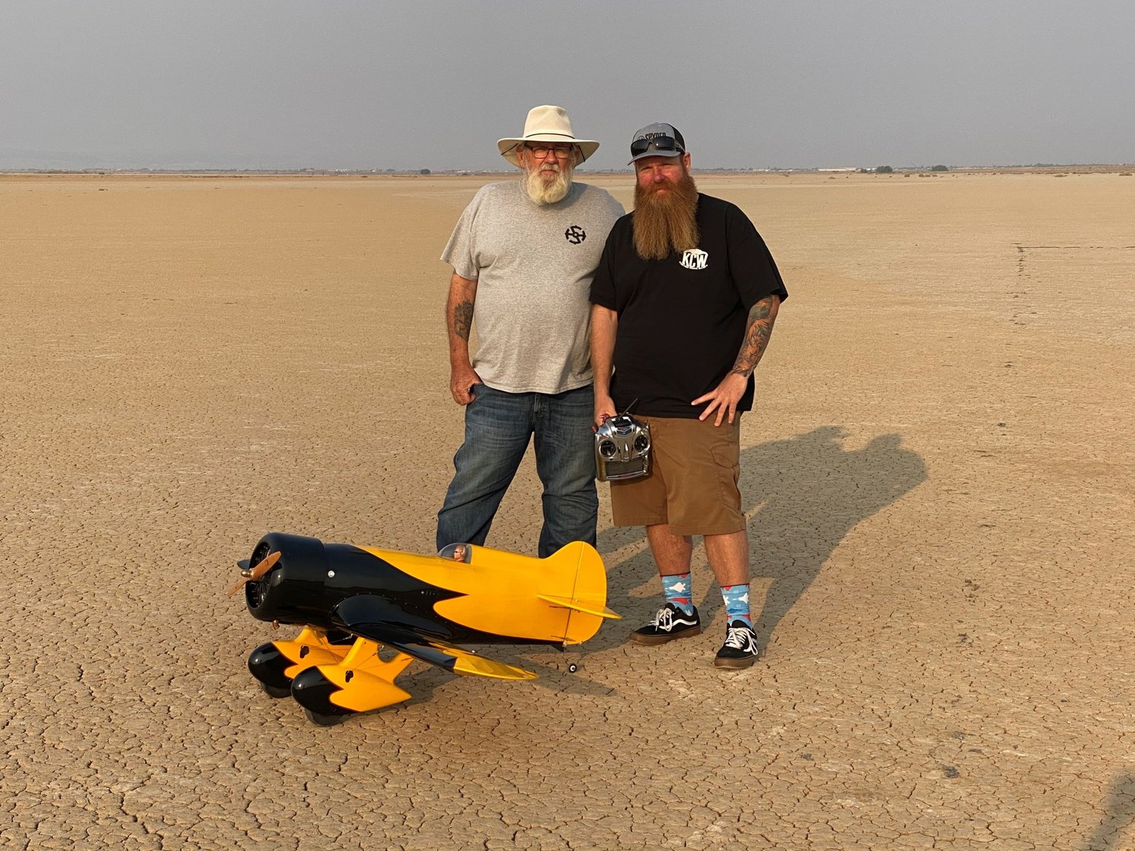 Two men stand by a yellow and black radio-controlled aircraft.