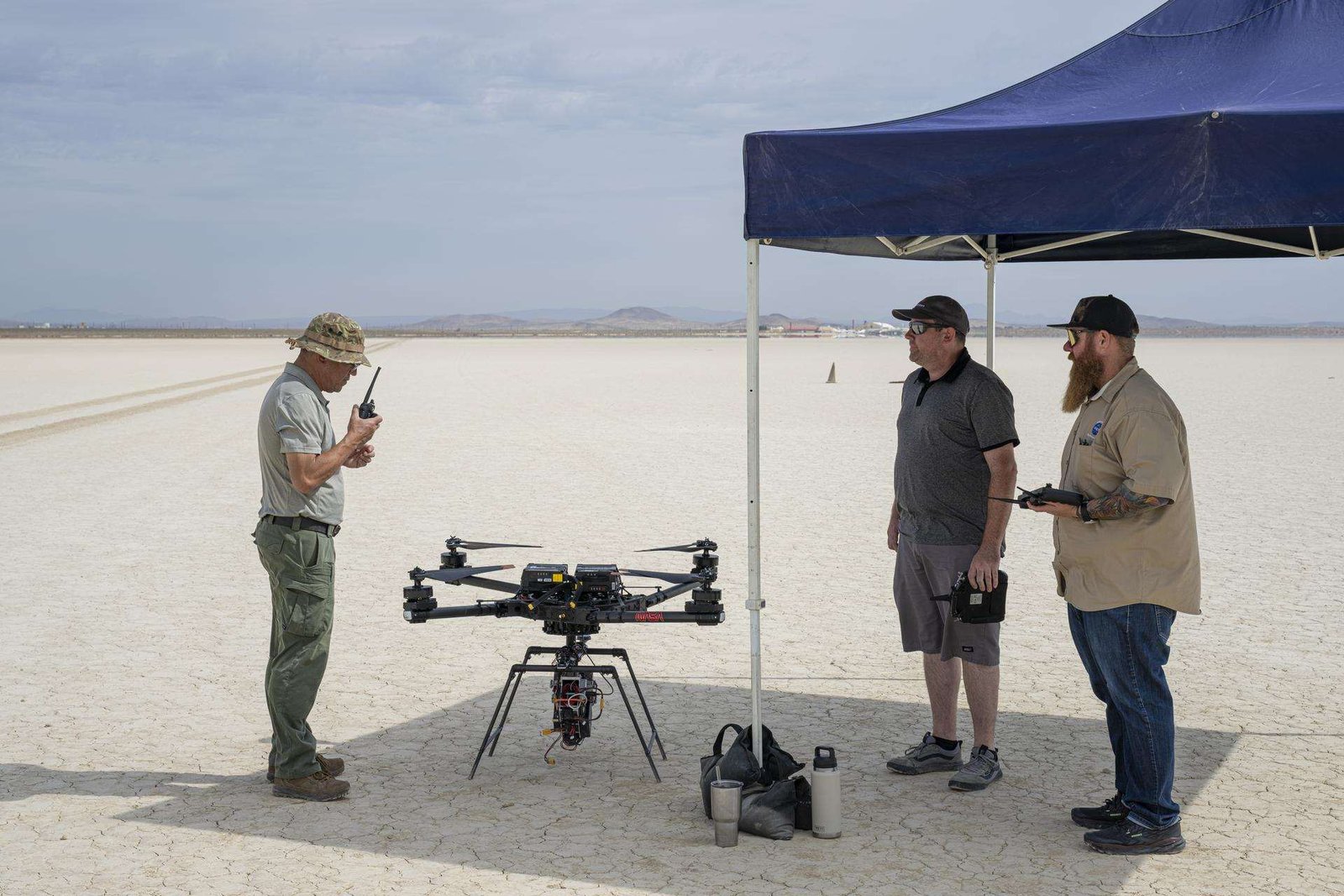 One man communicates with a hand-held radio, as two other men wait to the side for the go-ahead command to fly an experiment on a drone.