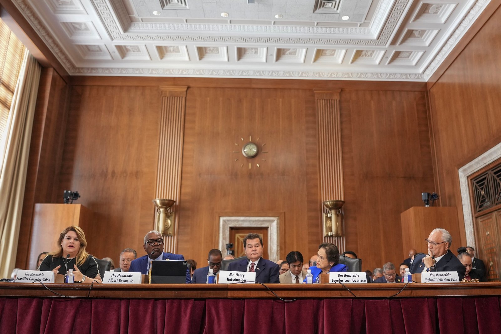 a group of people sit behind a long desk in a wood-paneled room