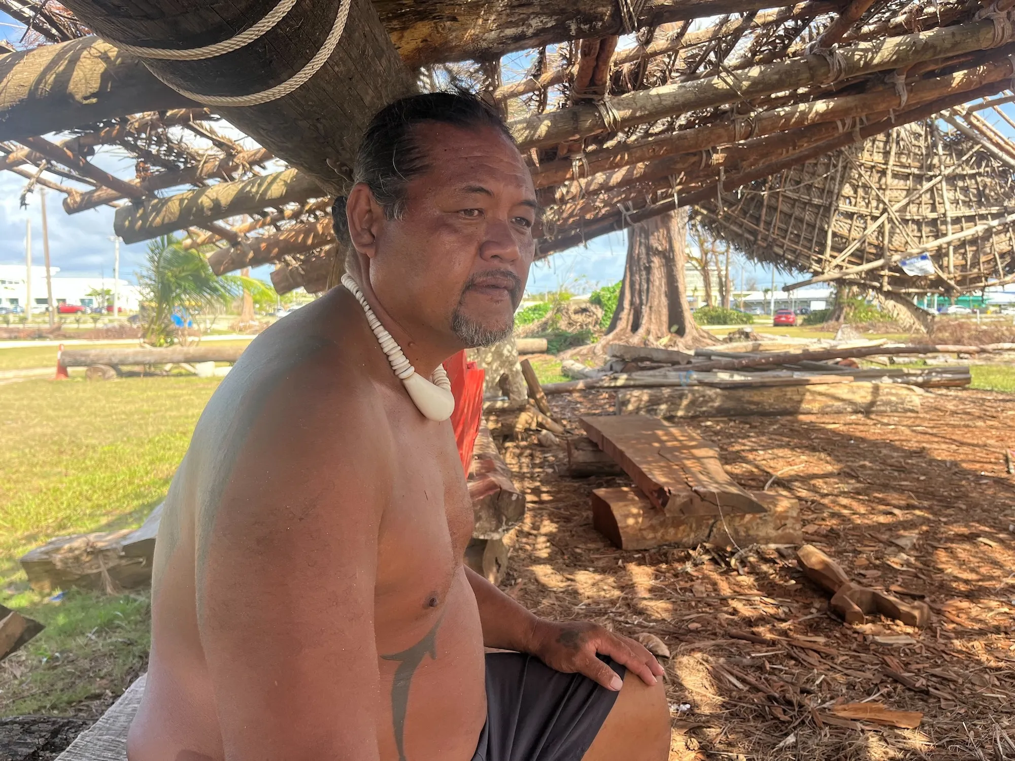 A man sits under a shelter made of natural materials