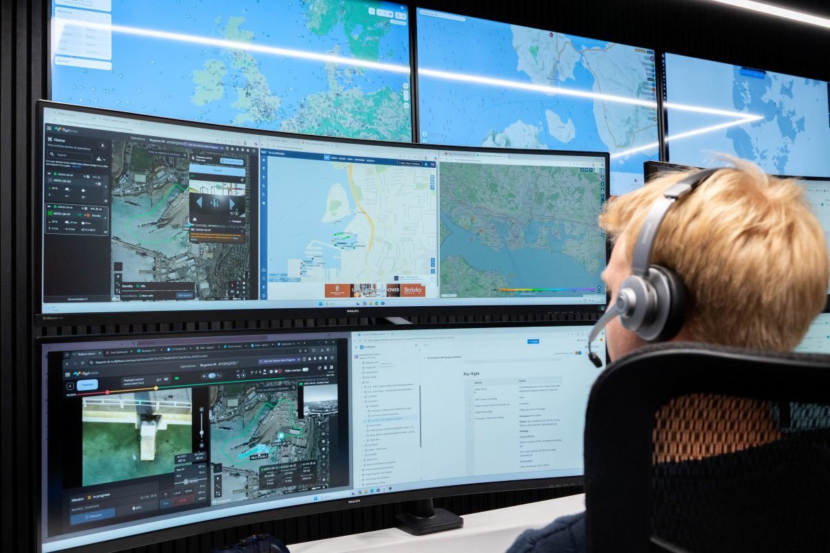 Drone operator wearing a headset at a remote operations centre, facing multiple mapping and flight-control screens