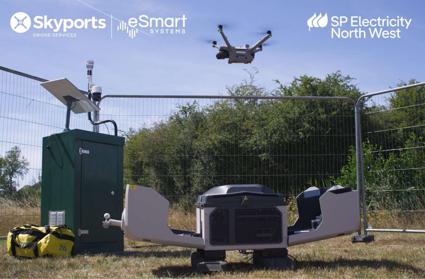 Drone flying above an automated docking station and monitoring equipment at a fenced outdoor site