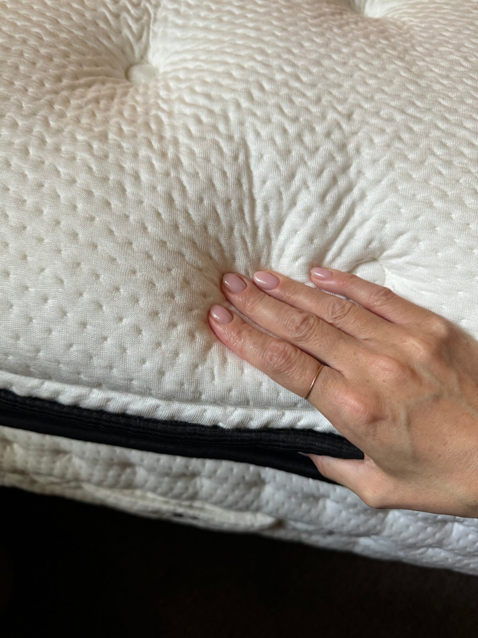 A hand pressing down on a white, quilted mattress surface with visible tufted buttons and a black zipper along the edge.