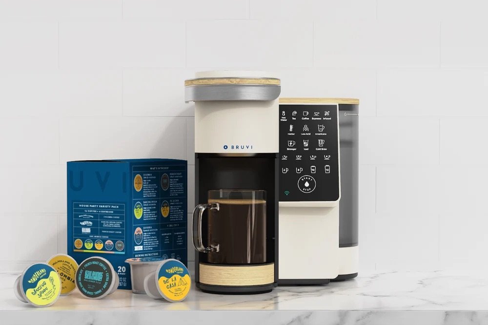 Single-serve coffee maker with digital controls on a marble counter, next to a box and several coffee pods—perfect for upgrading your morning routine, especially during our Labor Day sale.