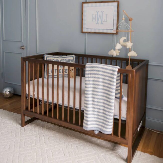 Wooden baby crib with a striped blanket draped over the side, cloud mobile, and monogram art on a blue wall in a nursery—perfect for your little one’s space, especially during our Labor Day Sale.