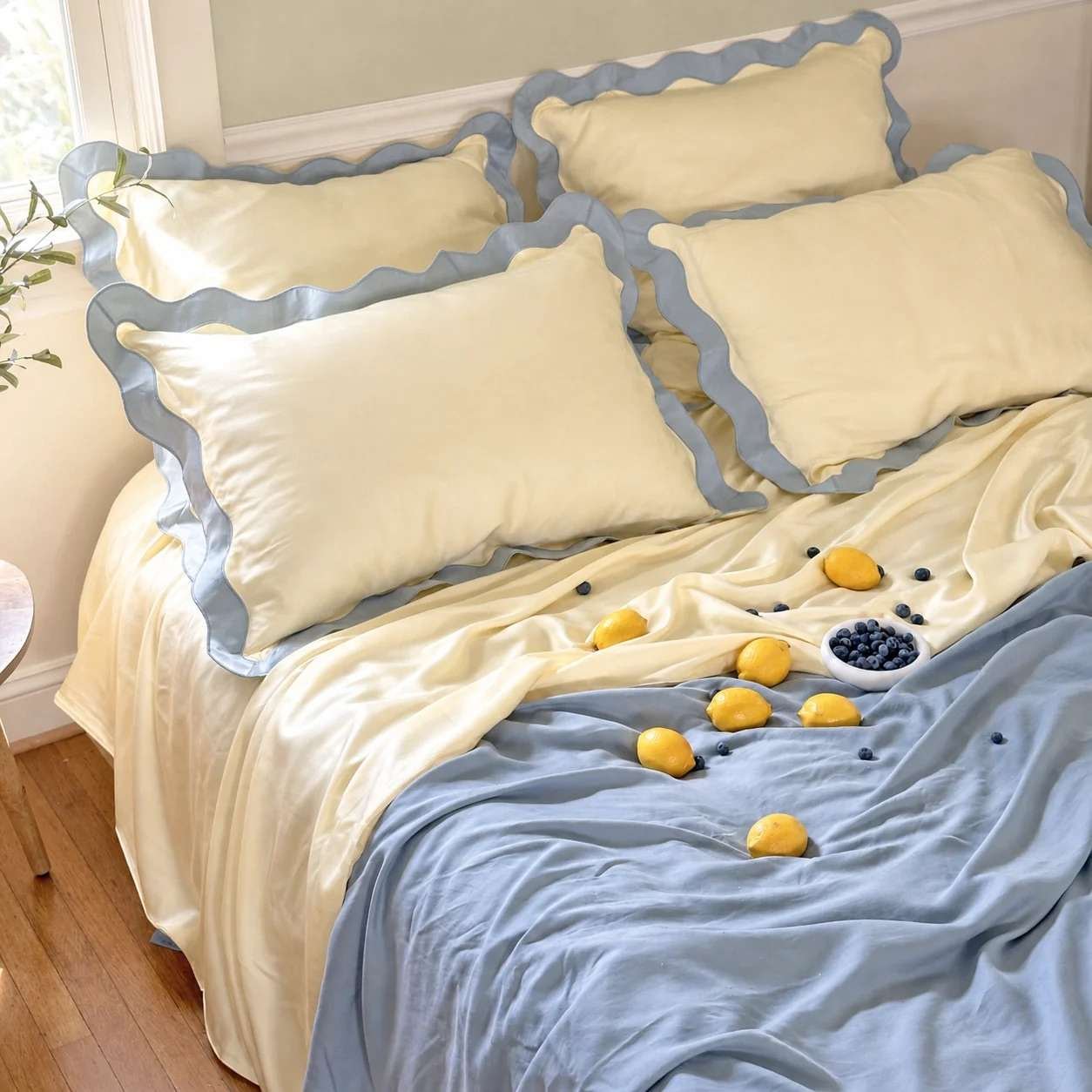 A bed with light yellow and blue wavy-edged pillows and bedding, scattered with whole lemons and blueberries on top—perfect for refreshing your space during our Labor Day Sale.