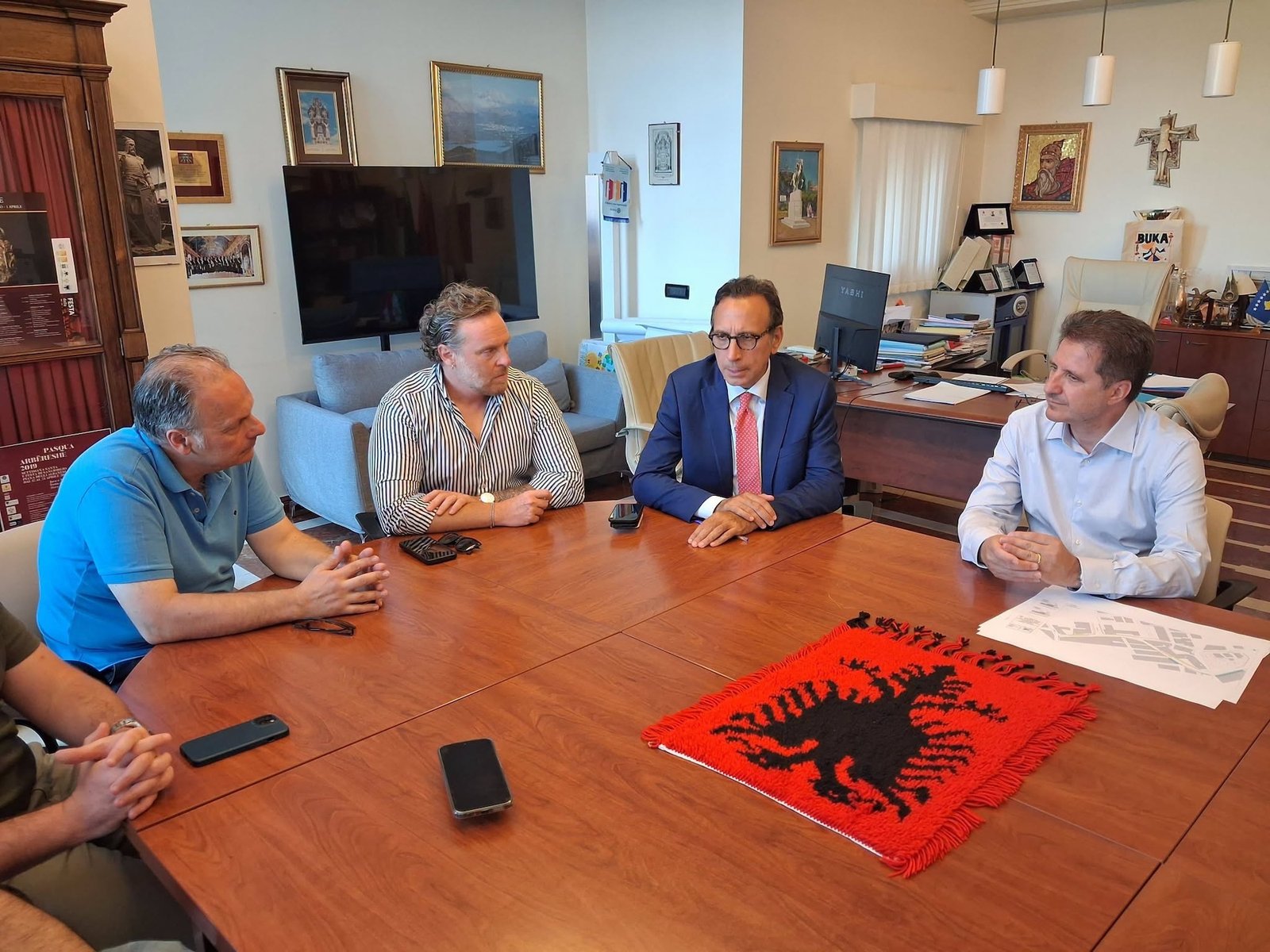 Men gather around a table with an Arbreshe symbol in the center